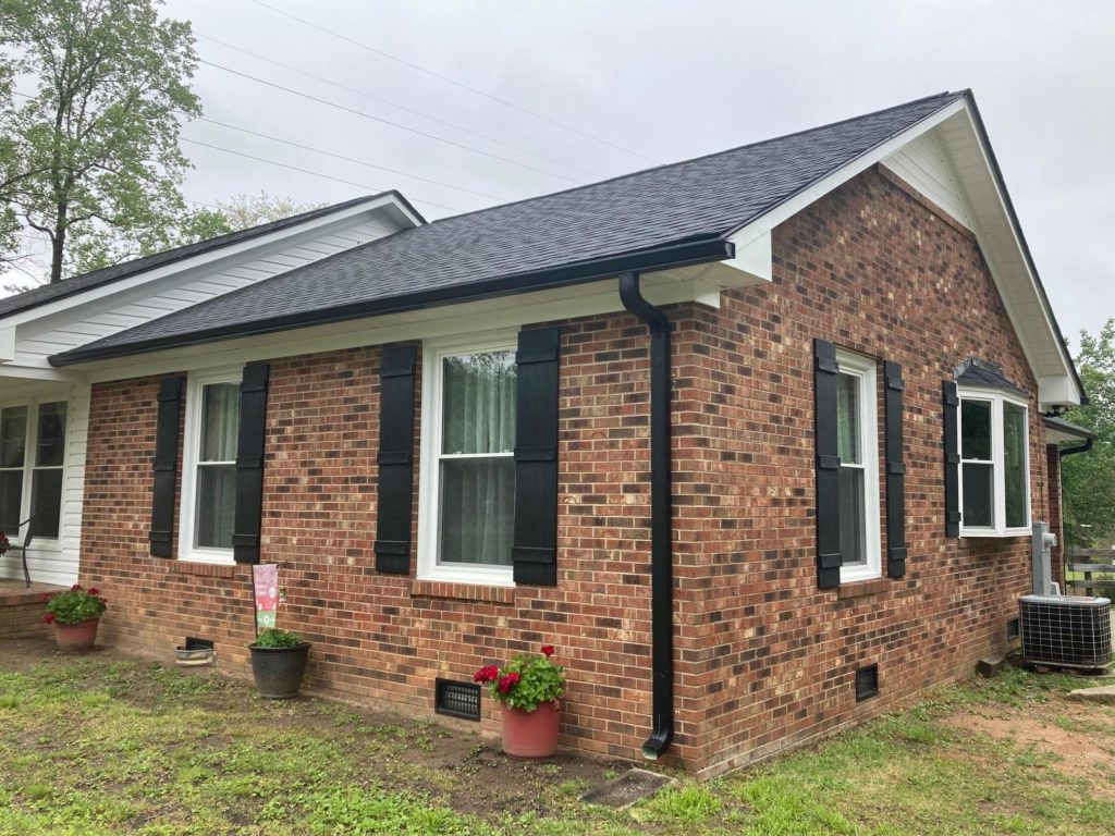 Brick house with black gutters and black shingle roof